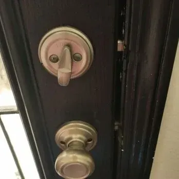 Close-up of a black door with a doorknob and deadbolt in a silver finish, partially open.