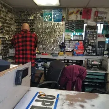 Man in a red plaid shirt at a locksmith shop, standing near key racks and a counter.