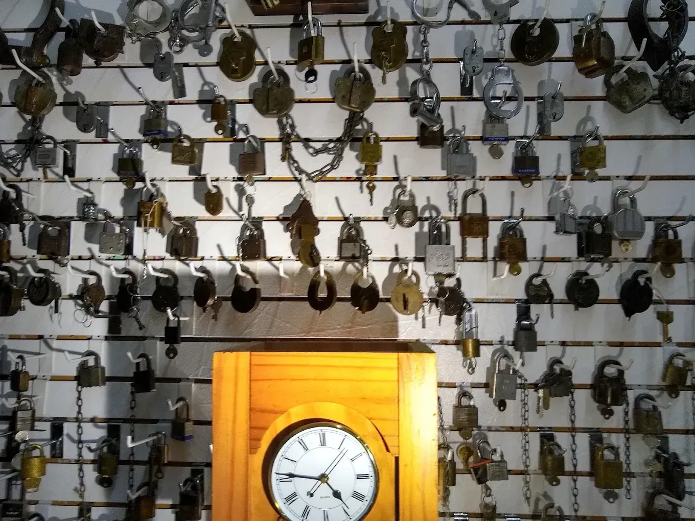 Wall display of antique locks and keys, with a wooden clock in the foreground.