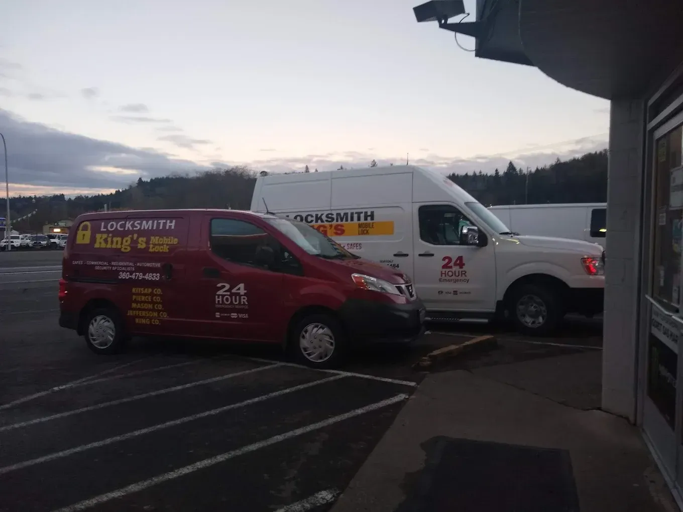 Two locksmith vans parked in front of a store. One red, one white.