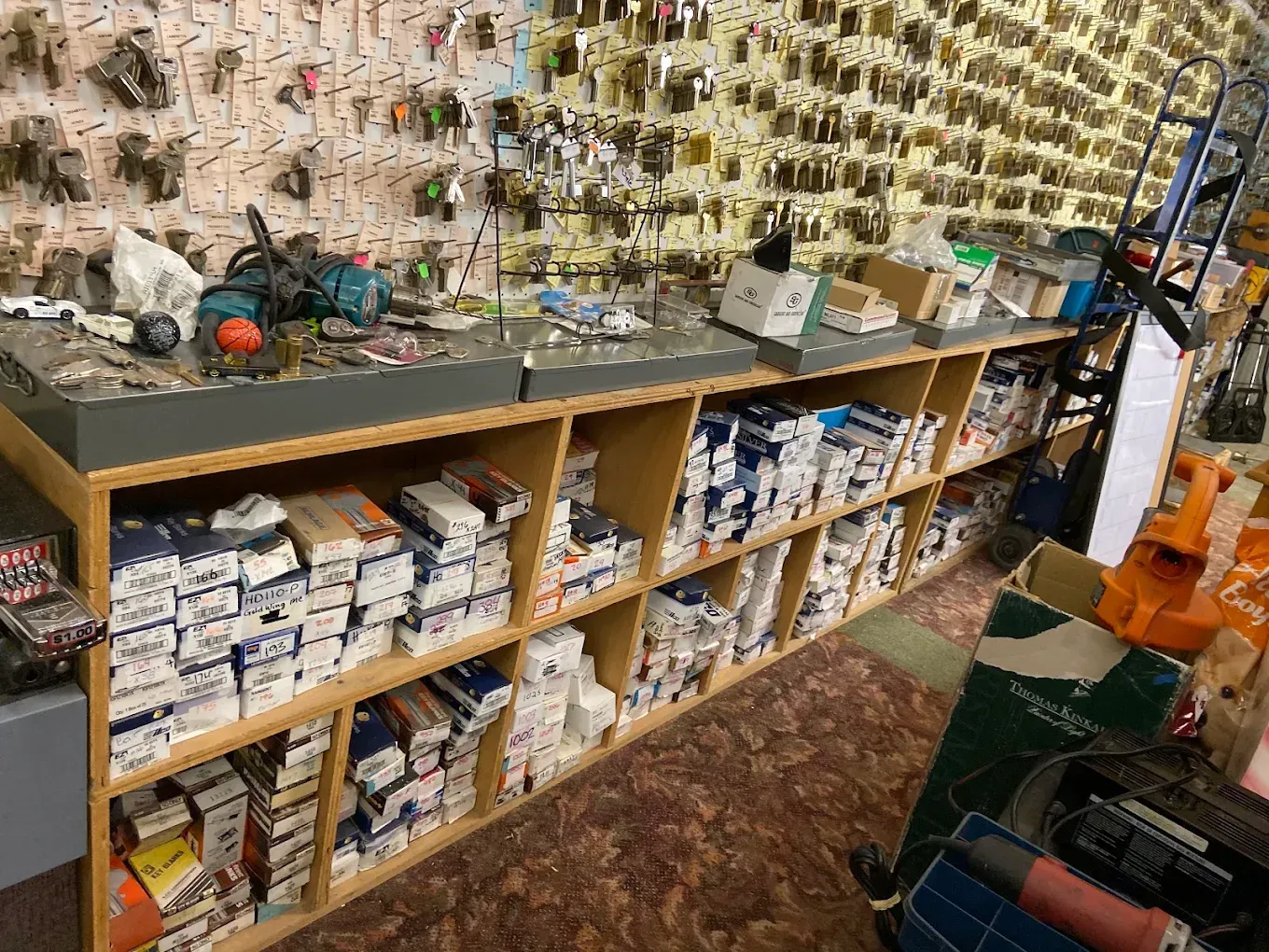 A key-cutting counter in a hardware store; keys hang on the wall, and parts are stored in boxes on shelves below.