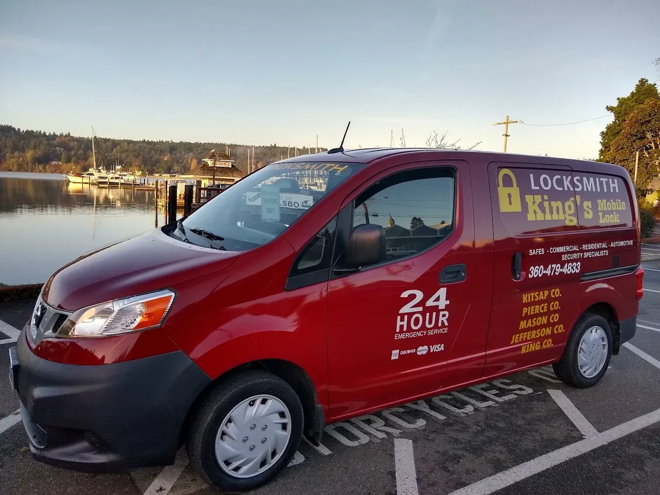 Red locksmith van parked near water, advertising 24-hour service.