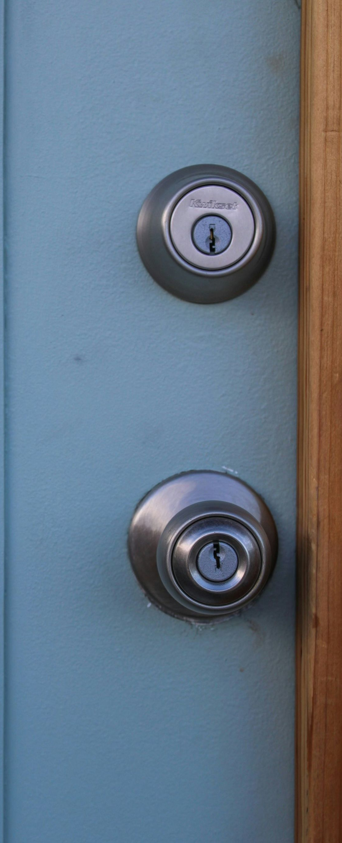 Two silver door locks on a blue door next to a wooden frame