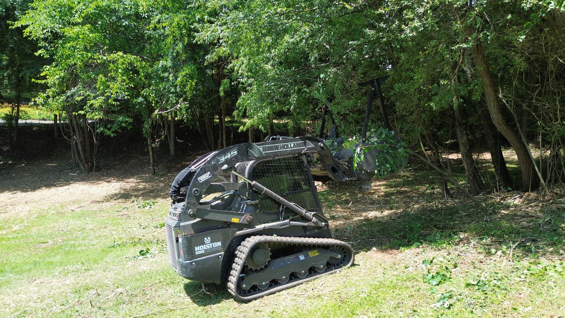 Small black tracked robot on grass near trees in a park-like setting