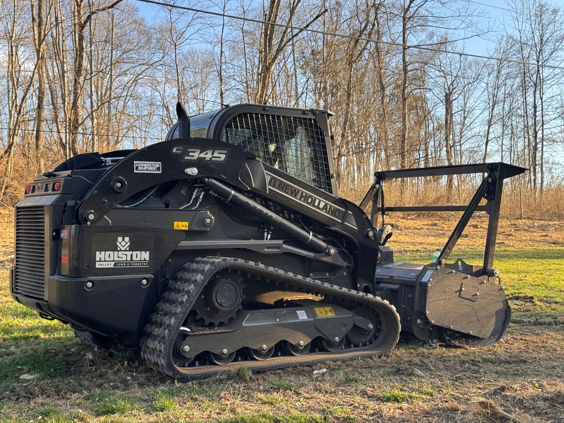 Black tracked skid steer loader with bucket in a wooded field, side view