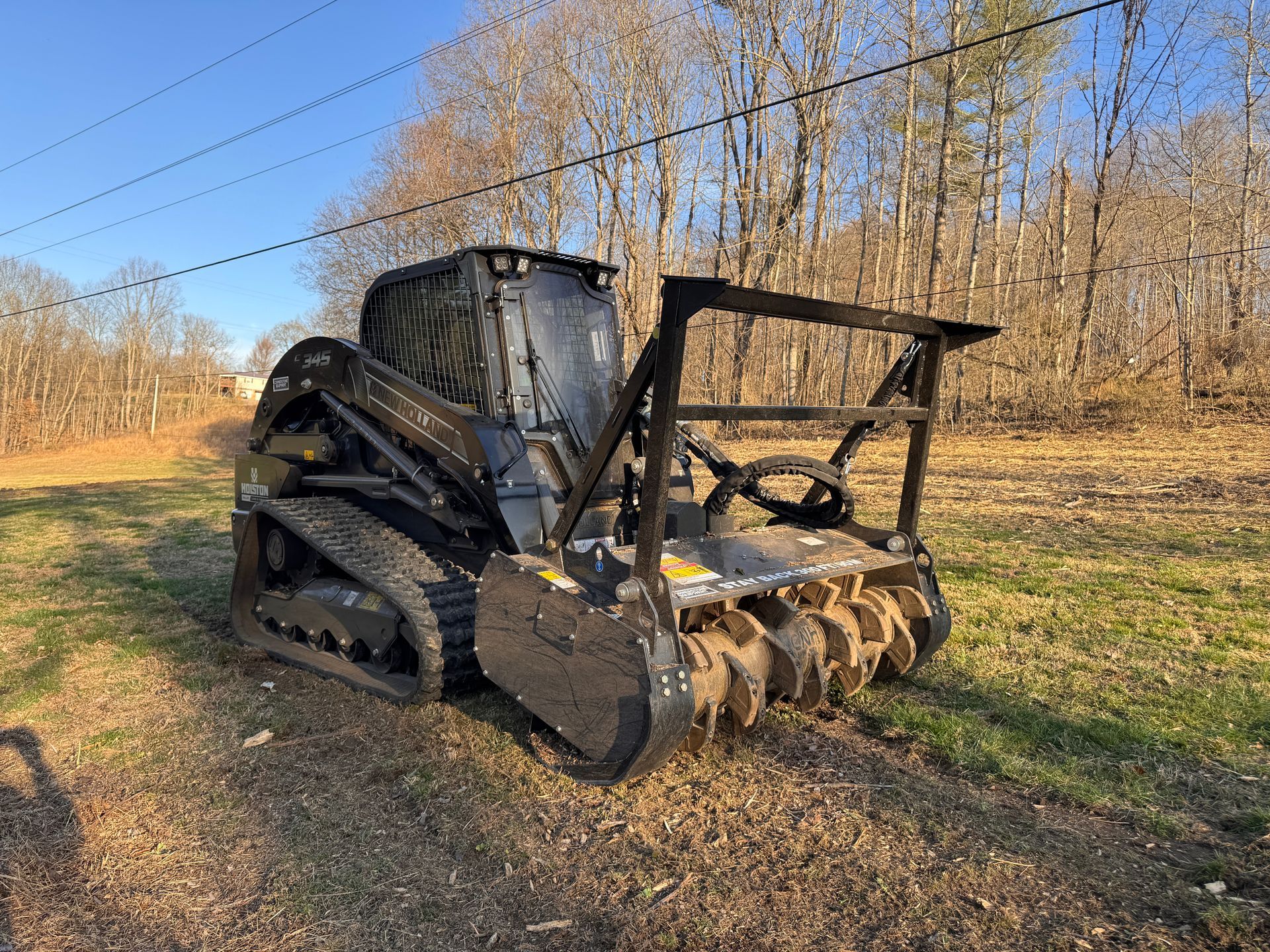 Black tracked forestry machine with cutting blade in a field under a clear blue sky