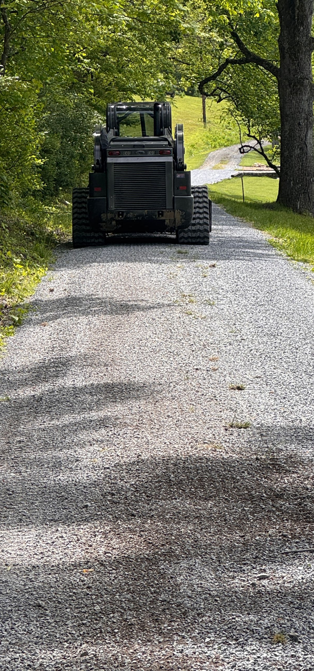 Black construction vehicle on a gravel path under green trees