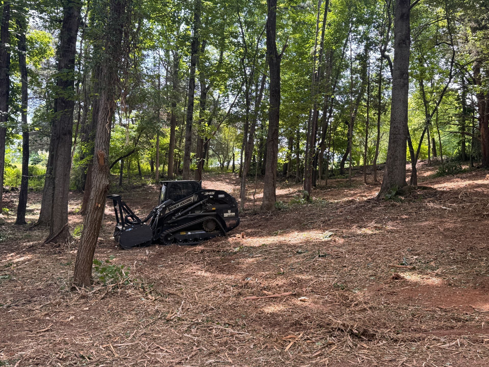 A black overturned vehicle in a wooded area with trees and dry ground.