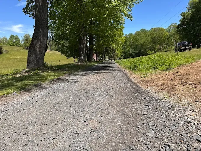 Gravel path through a green park with tall trees and a parked vehicle in the distance