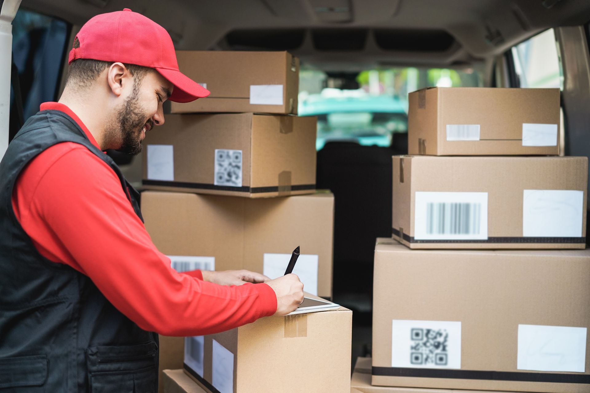 Delivery worker in red cap loading labeled boxes into a van