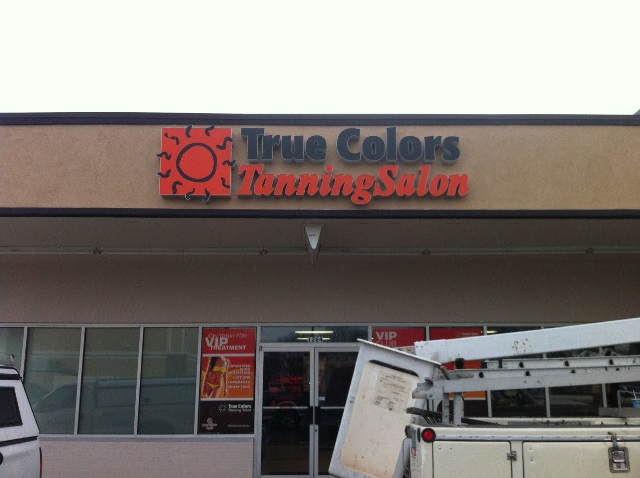 The storefront of True Colors Tanning Salon with an orange sun logo and the business name above the glass entrance doors.