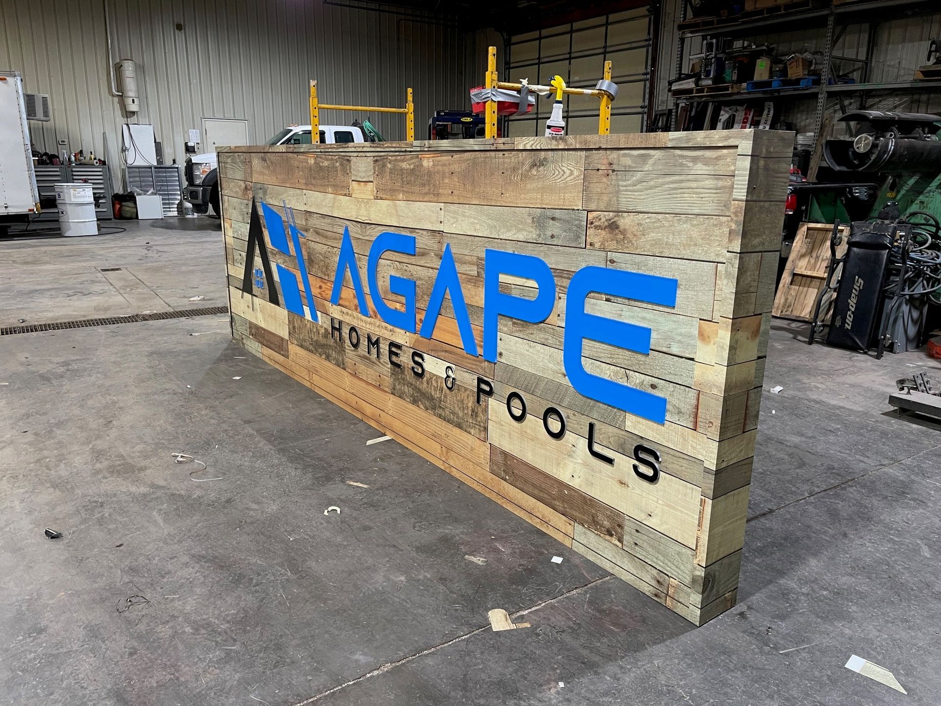A large wooden sign for agape homes & pools is sitting on the ground in a garage.