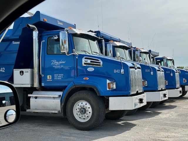 A row of blue dump trucks are parked in a parking lot