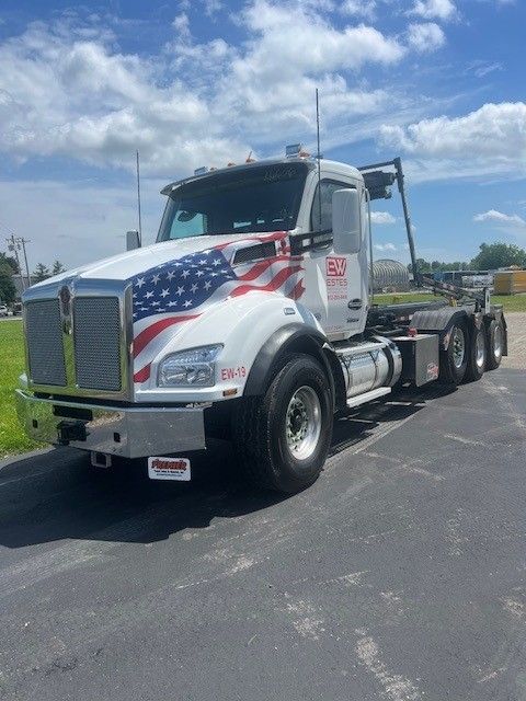 A white semi truck with an american flag on the front is parked on the side of the road.