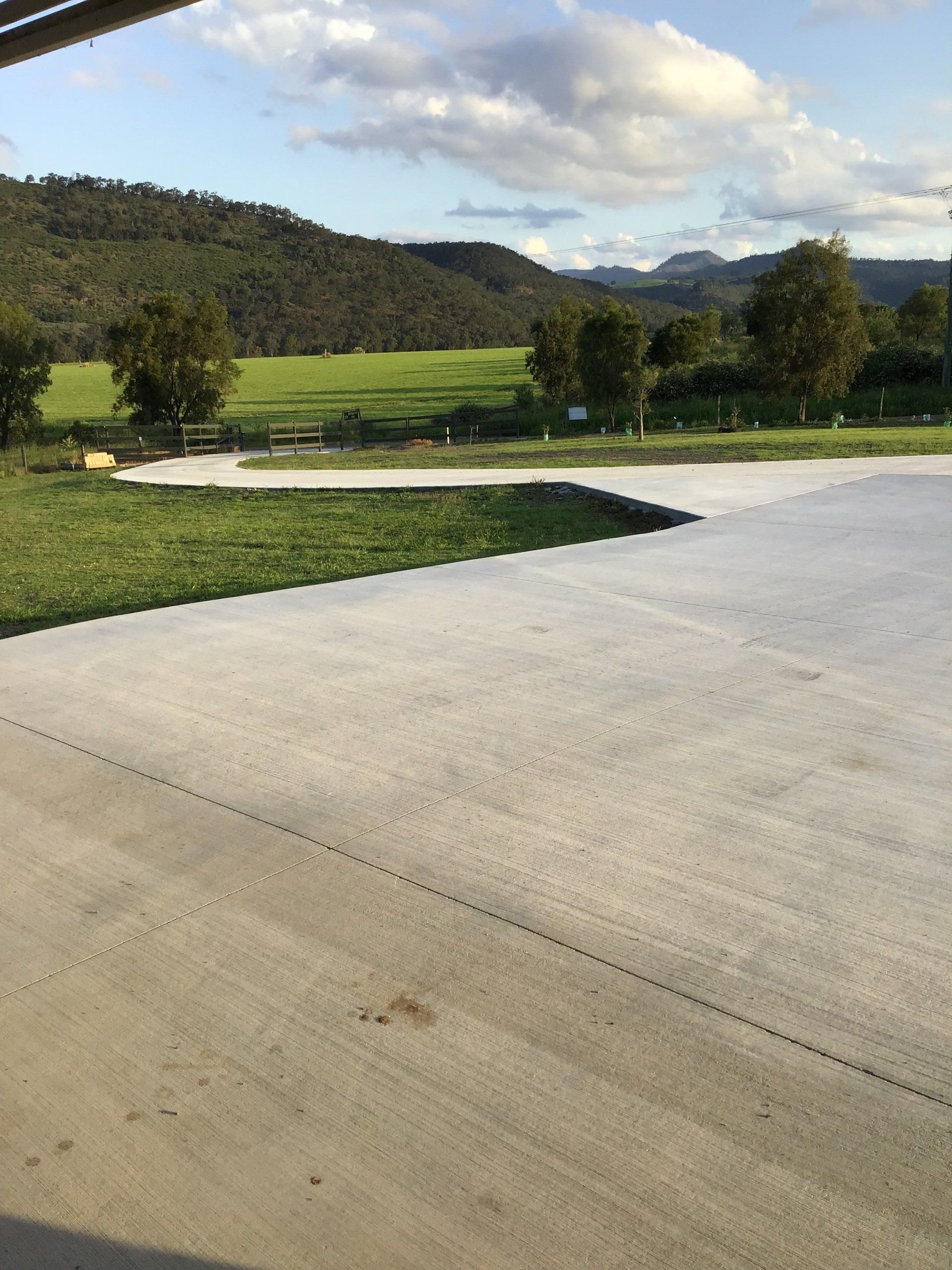 A Concrete Driveway Leading to a Grassy Field With Mountains in the Background — C R Concreting in Pittsworth, QLD