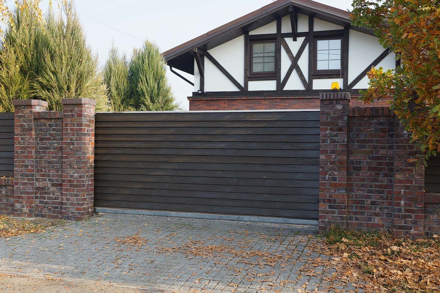 Un mur de briques avec un portail coulissant devant une maison.