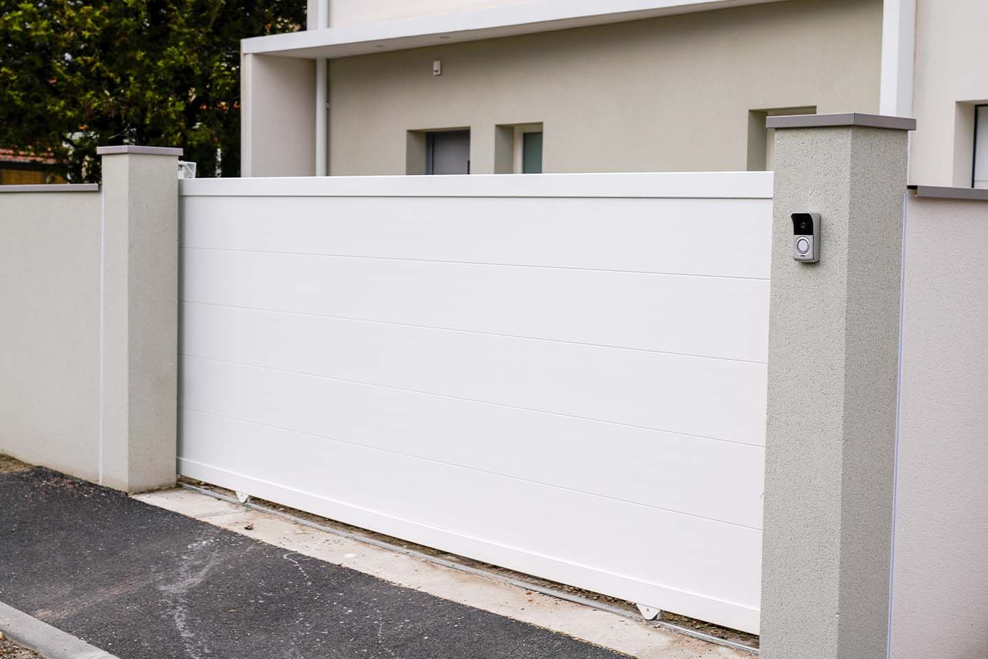 Un portail coulissant blanc se trouve devant une maison.