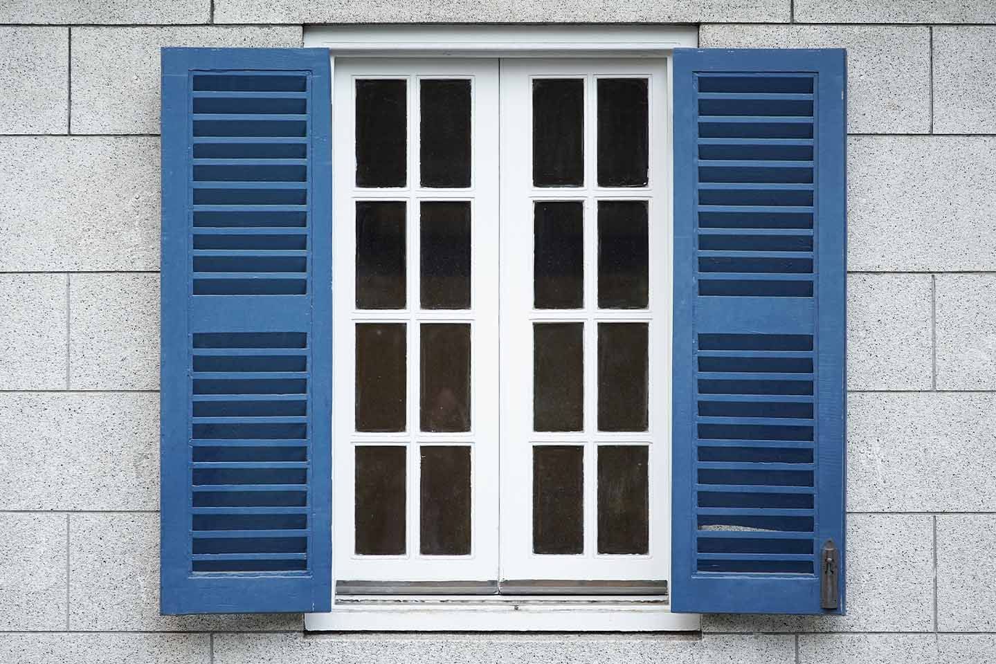 Une fenêtre blanche avec des volets bleus sur un mur de briques.