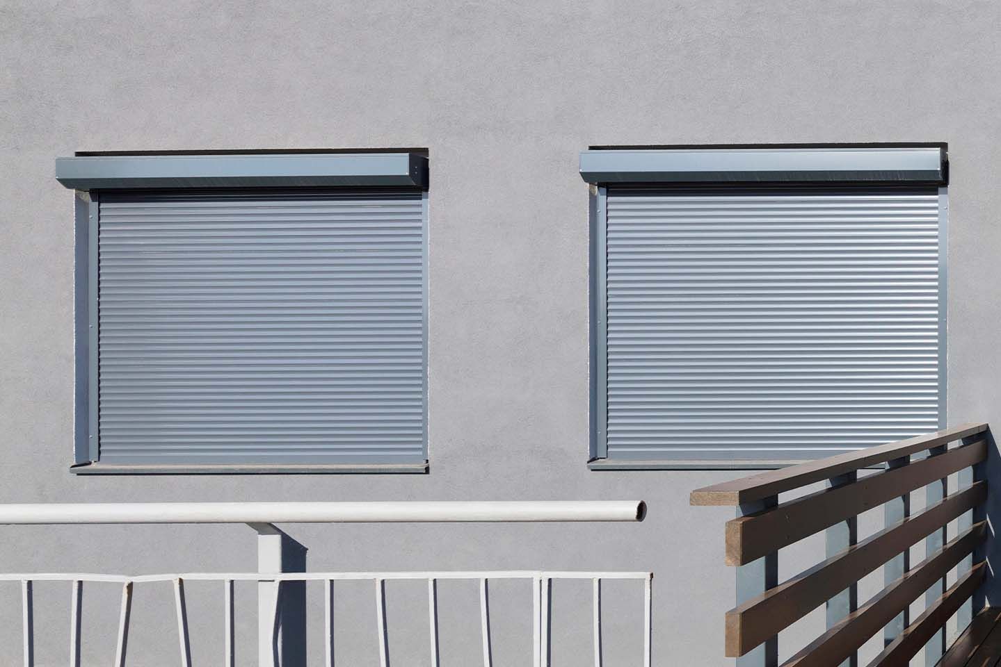 Un immeuble avec un balcon et deux fenêtres avec volets roulants