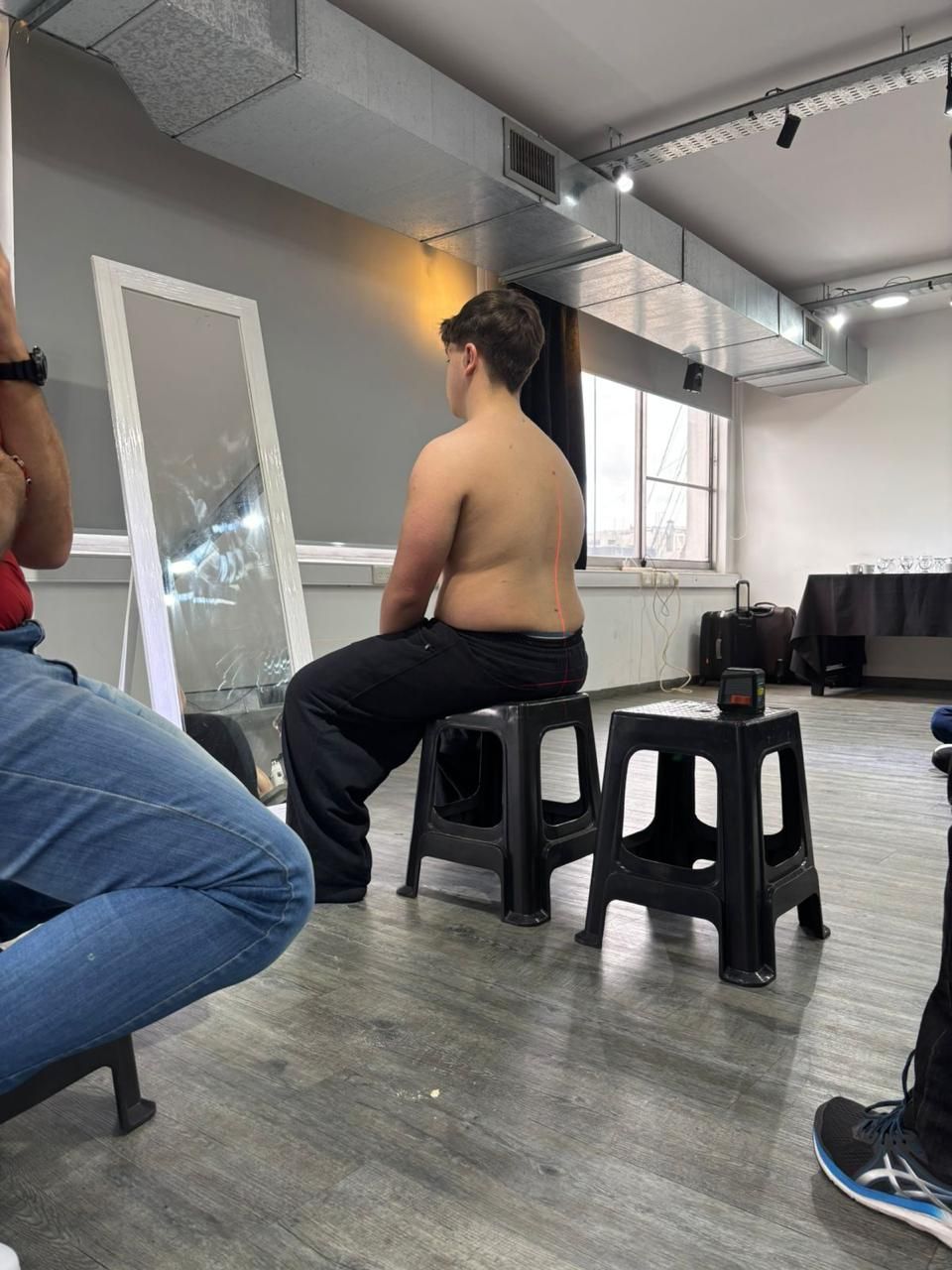 Personas sentadas en taburetes en un estudio con espejos, paredes grises y conductos de ventilación a la vista.