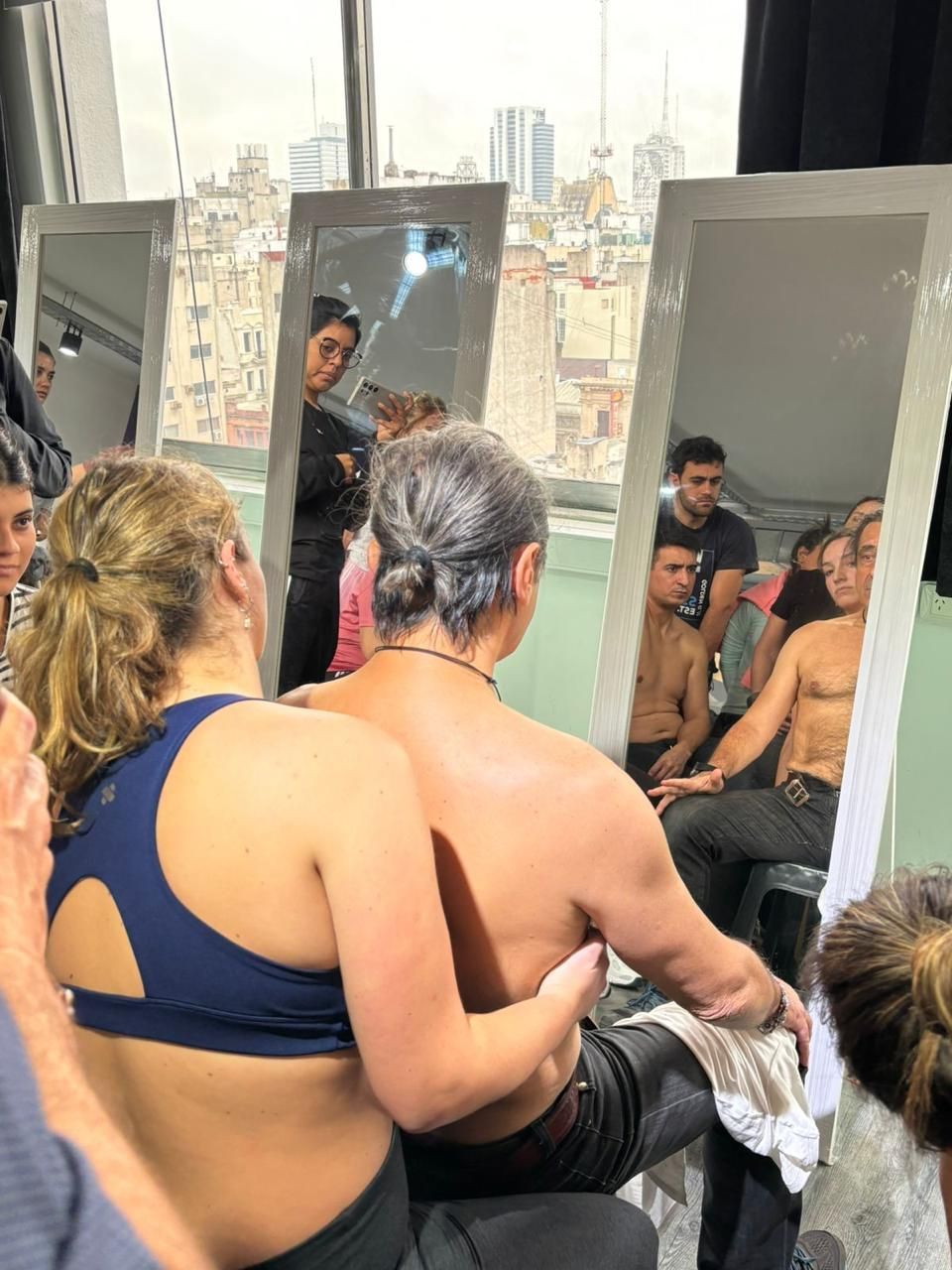 Varias personas se sientan juntas en una habitación con espejos, mirándose unas a otras en una conversación grupal íntima.
