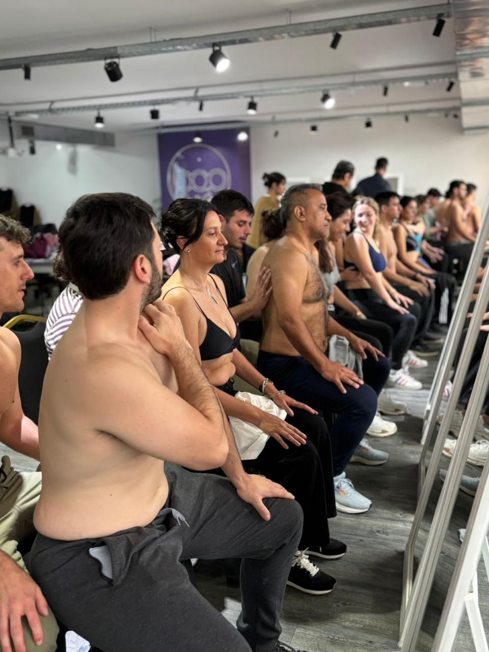 Personas sentadas en un estudio, mirando al frente con los brazos cruzados durante una clase de entrenamiento grupal.