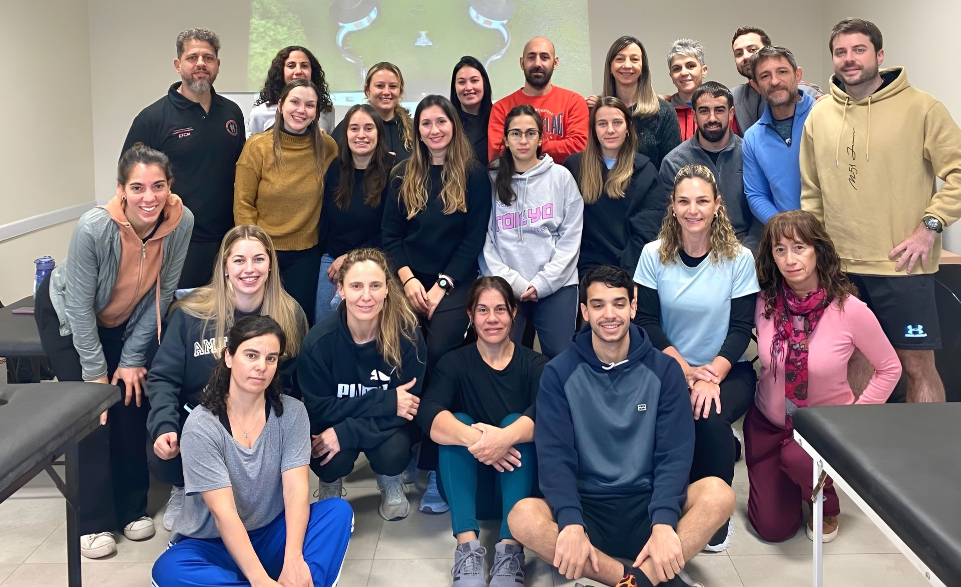 Grupo de personas posando en el interior de un aula, sentadas y de pie frente a una pantalla de proyección.