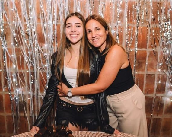Dos mujeres sonriendo y abrazándose frente a un telón de fondo de oropel plateado en una fiesta.