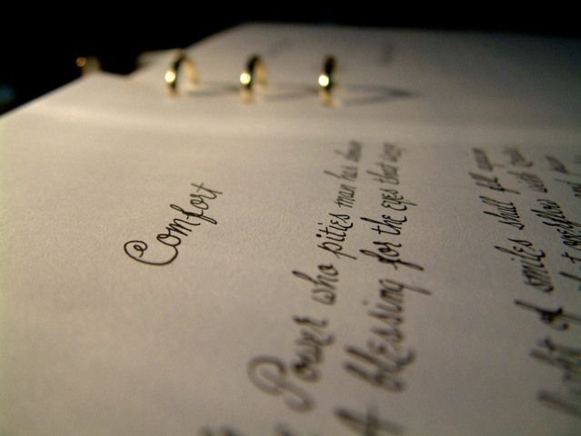 Close-up of a handwritten page under warm light, with metal rings at the top and blurred text in focus.
