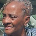 Smiling elderly person with short gray hair outdoors in sunlight