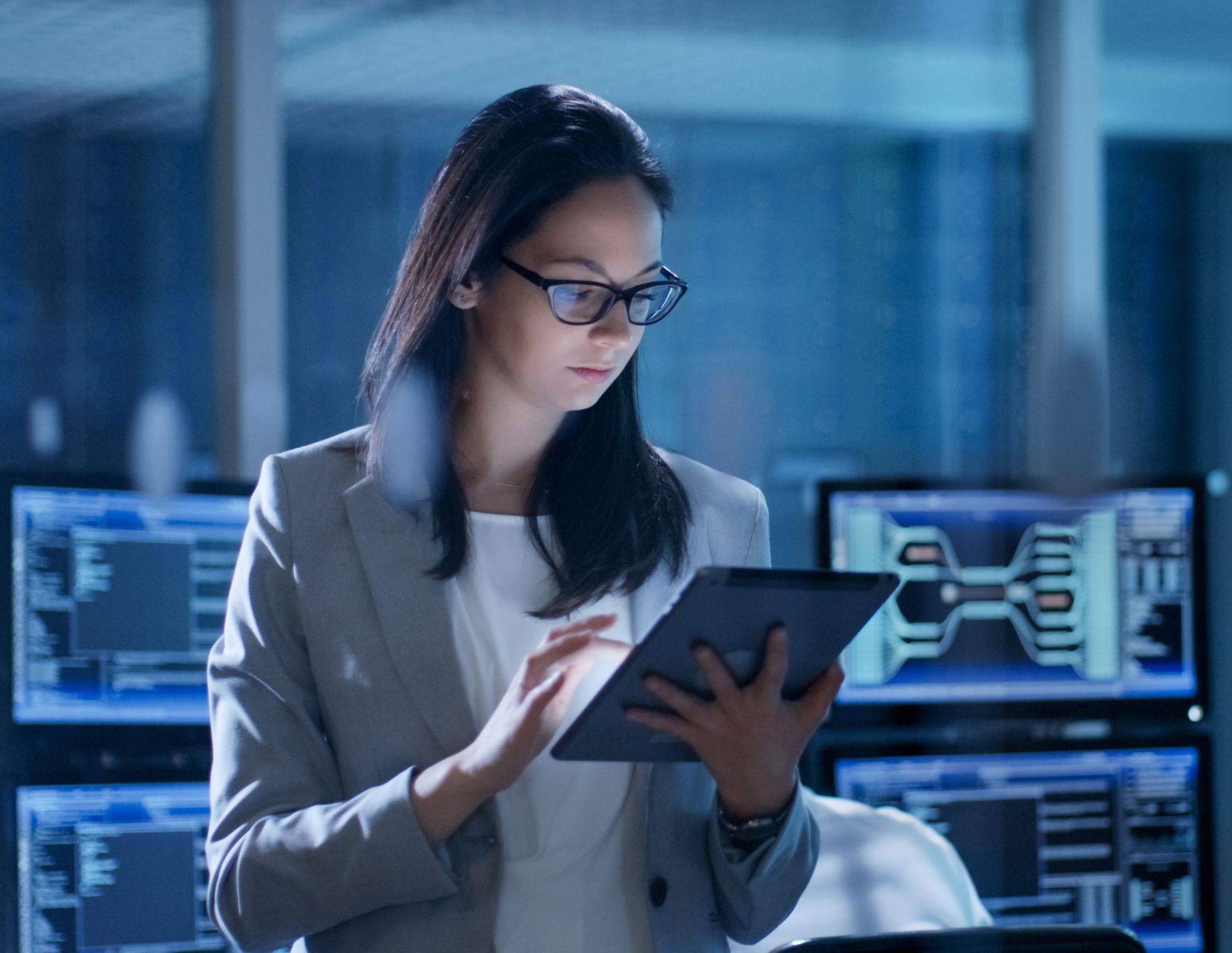 Professional woman using a tablet in a modern office with computer screens in the background