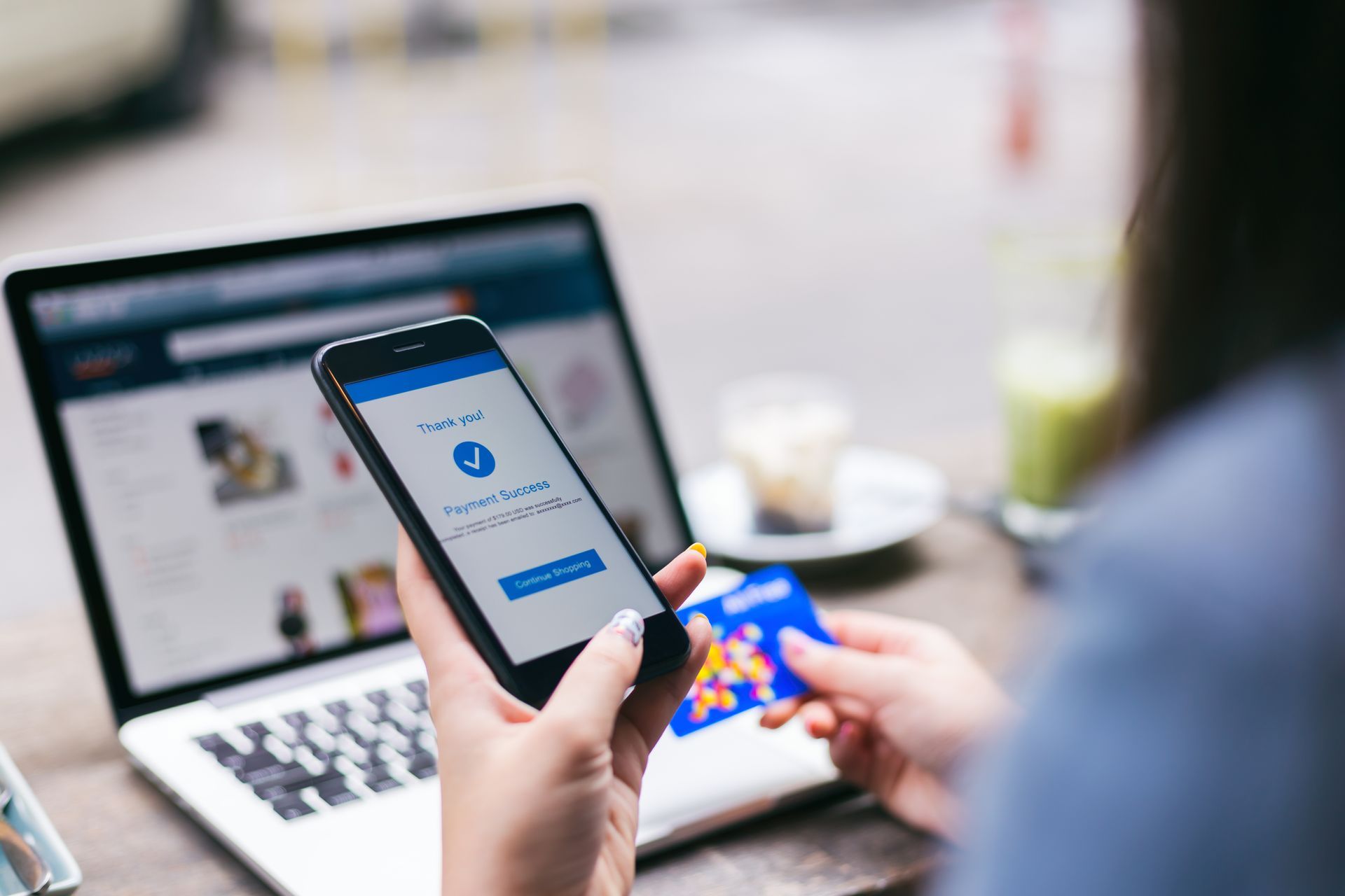 Person holding a smartphone with a social media login screen in front of a laptop on a desk