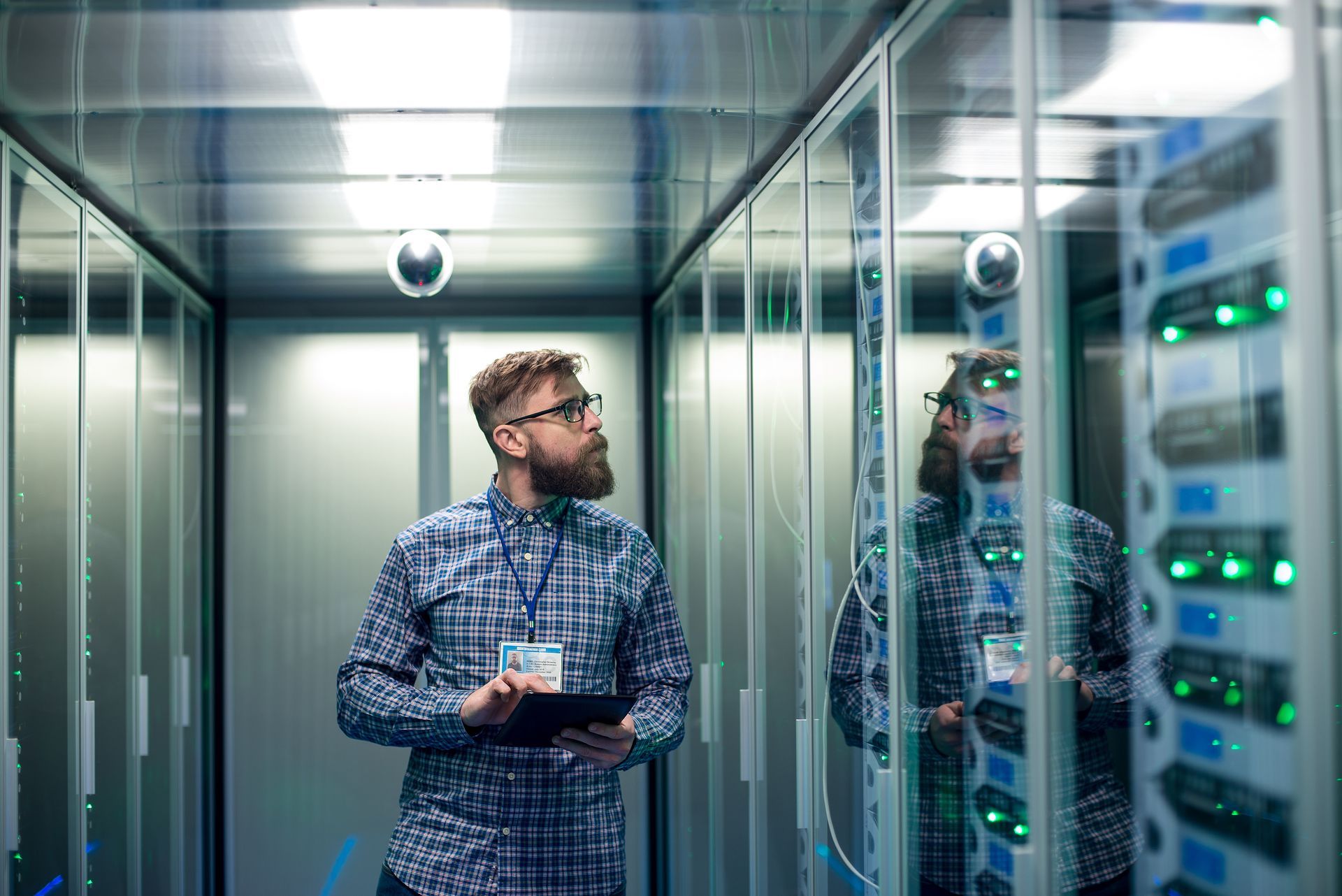 Technician in blue plaid shirt inspecting server racks in a data center corridor