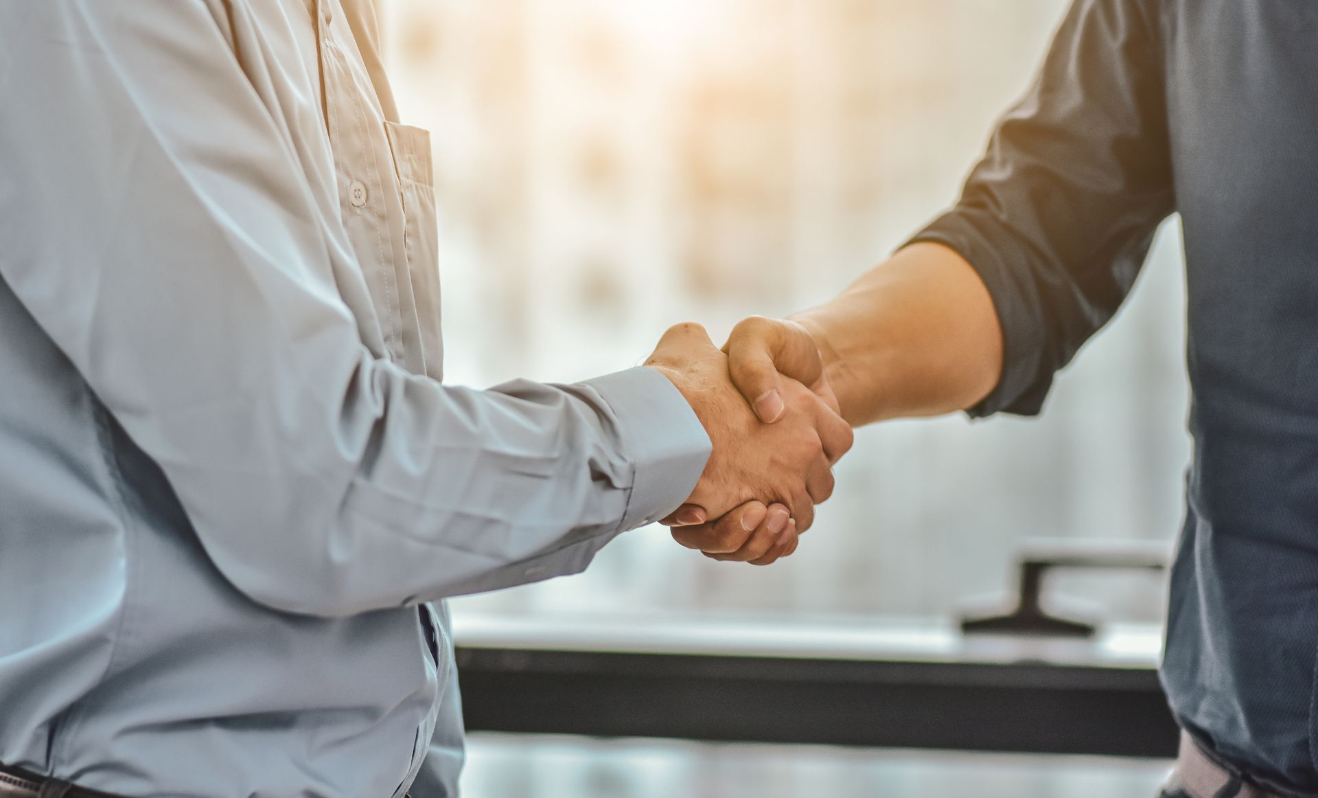 Two people in business attire shaking hands across a desk.