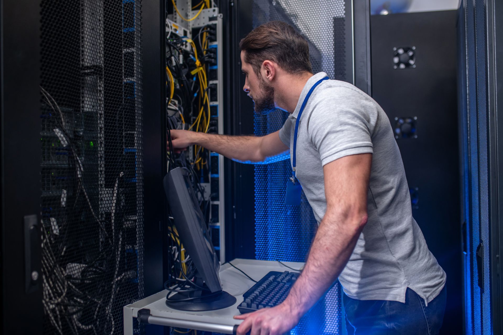 Technician in a server room reaching into a rack of network cables.