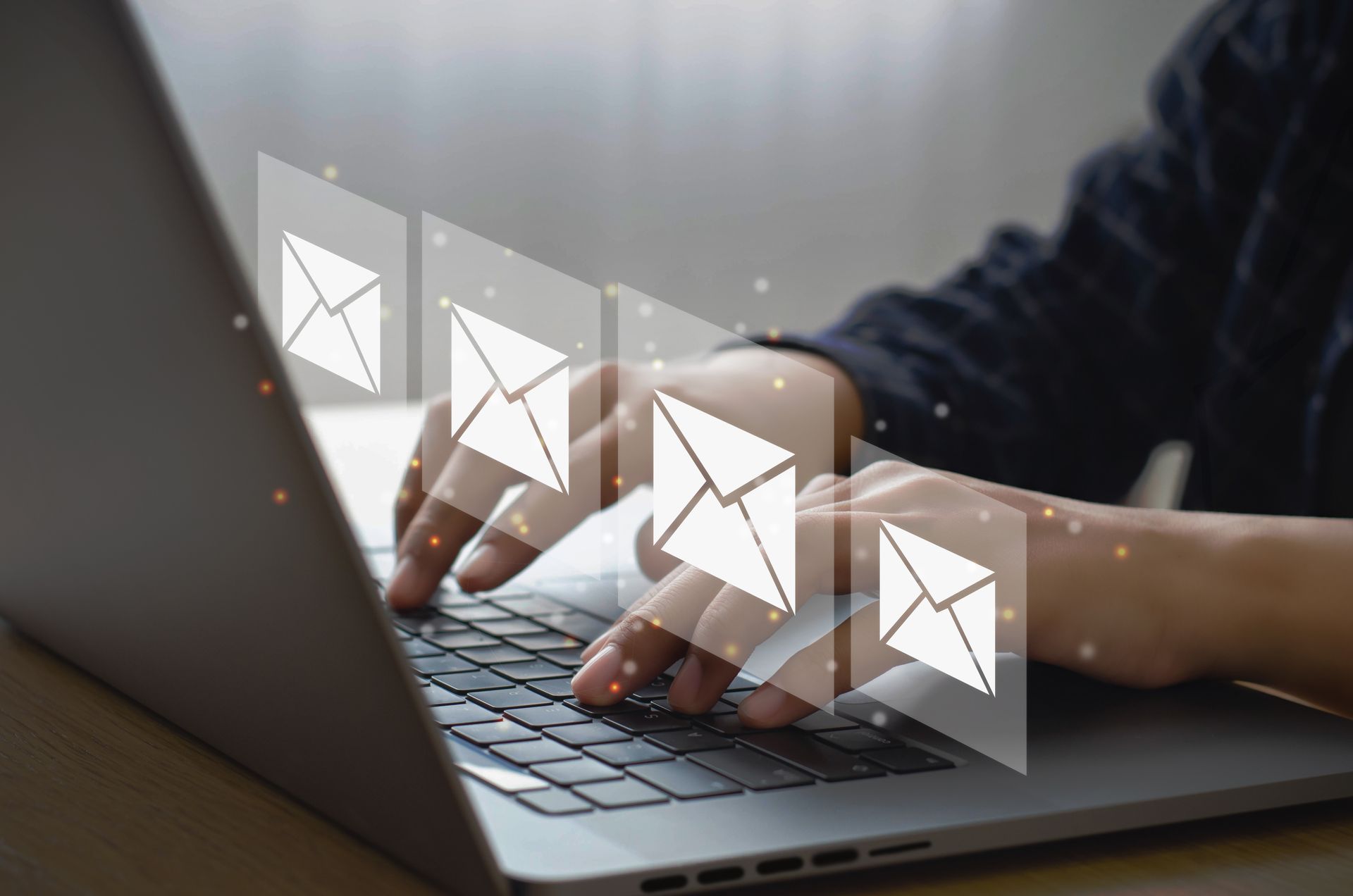Hands typing on a laptop with email icons floating above the keyboard