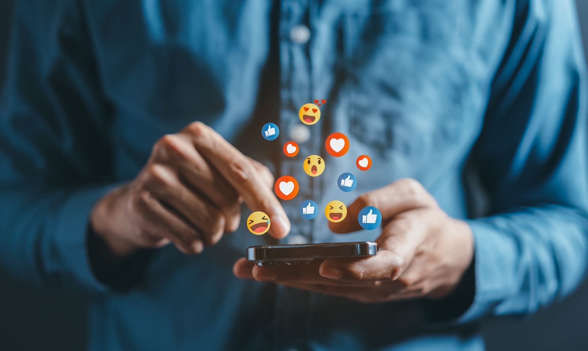 Hands typing on a smartphone with colorful social media reaction icons floating above it