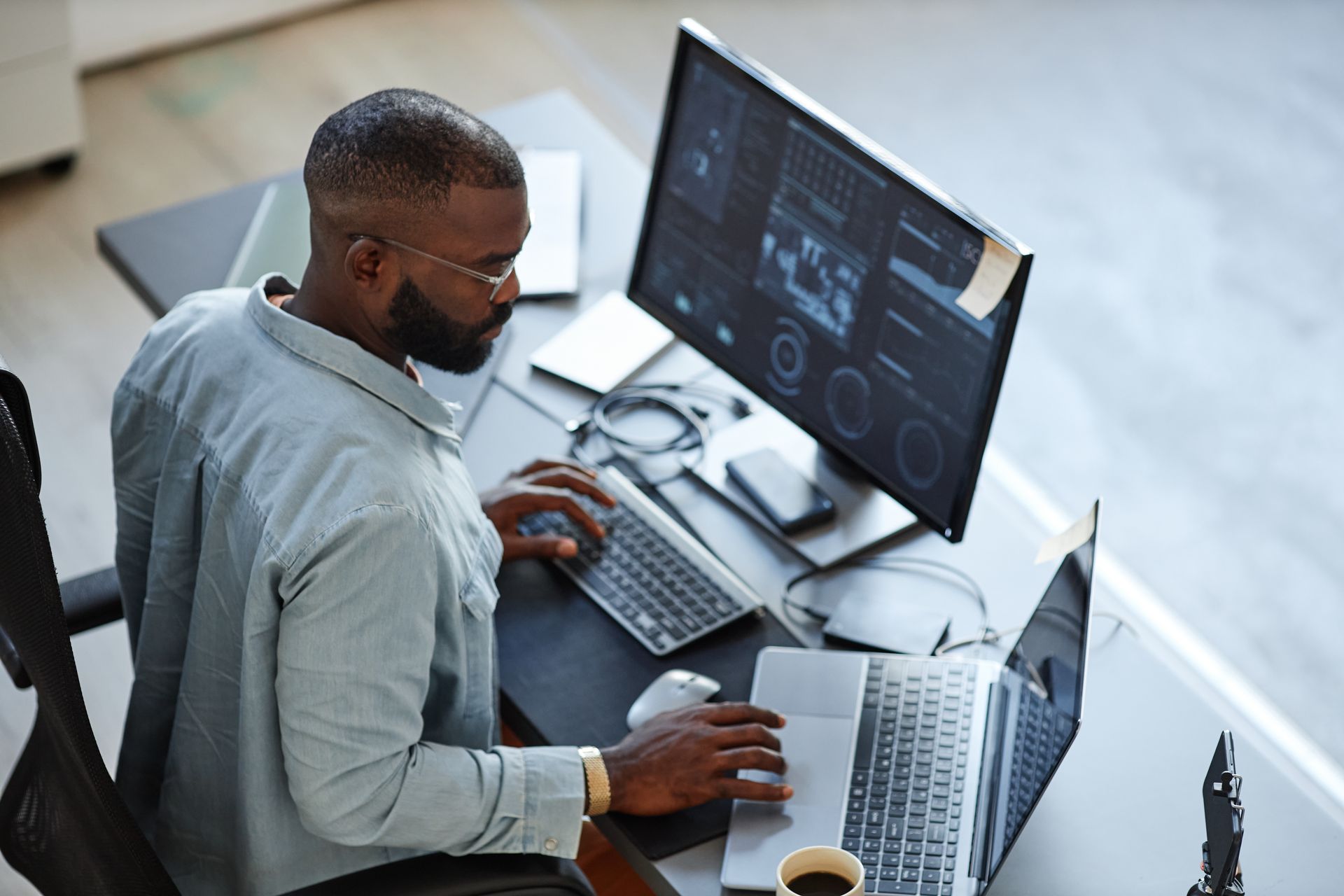 Person working at a desk with two monitors, typing on a keyboard and using a laptop in a modern office.