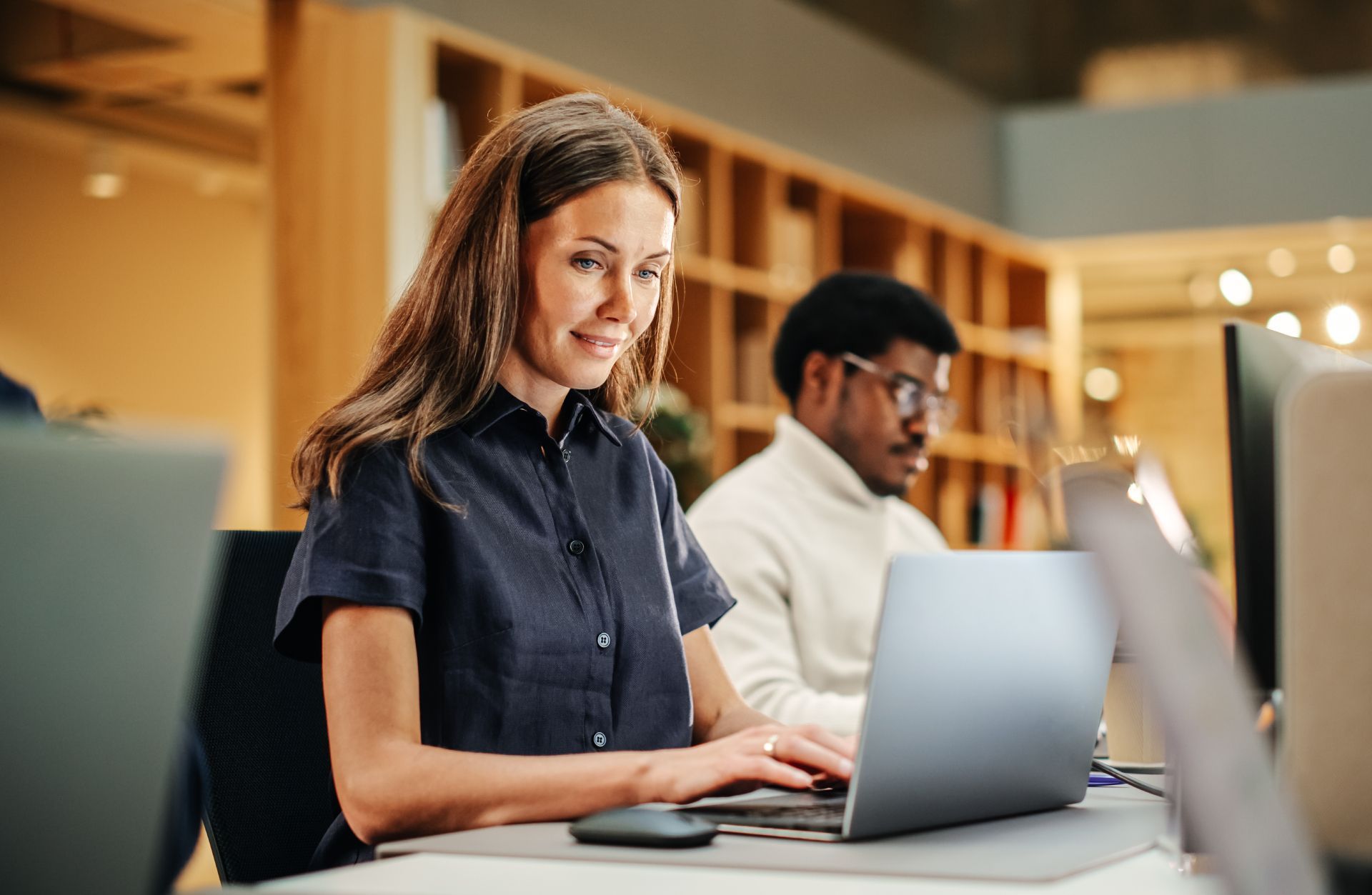 People working on laptops at a shared desk in a bright office library