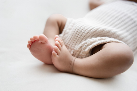 Slapende babyvoetjes gewikkeld in een beige gebreide deken op een witte ondergrond.