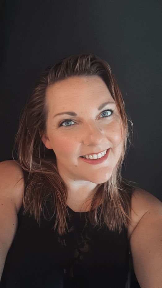 Lachende vrouw met golvend bruin haar in een zwarte top tegen een donkere achtergrond.