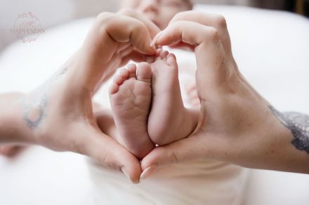 Volwassen handen vormen een hart rond de voetjes van een baby op een witte deken.