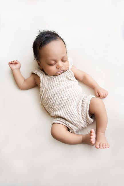 Slapende baby in een crèmekleurig gebreid rompertje, liggend op een witte achtergrond.