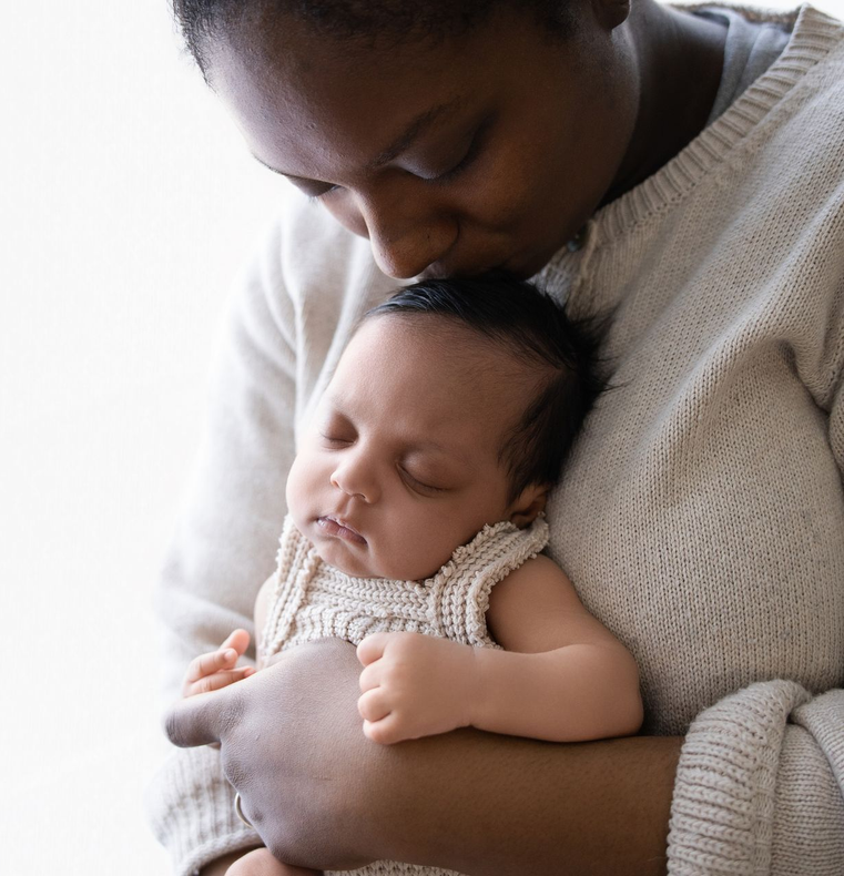 Een volwassene houdt een slapende baby vast en kust hem, terwijl de baby in een zachte gebreide trui is gewikkeld.