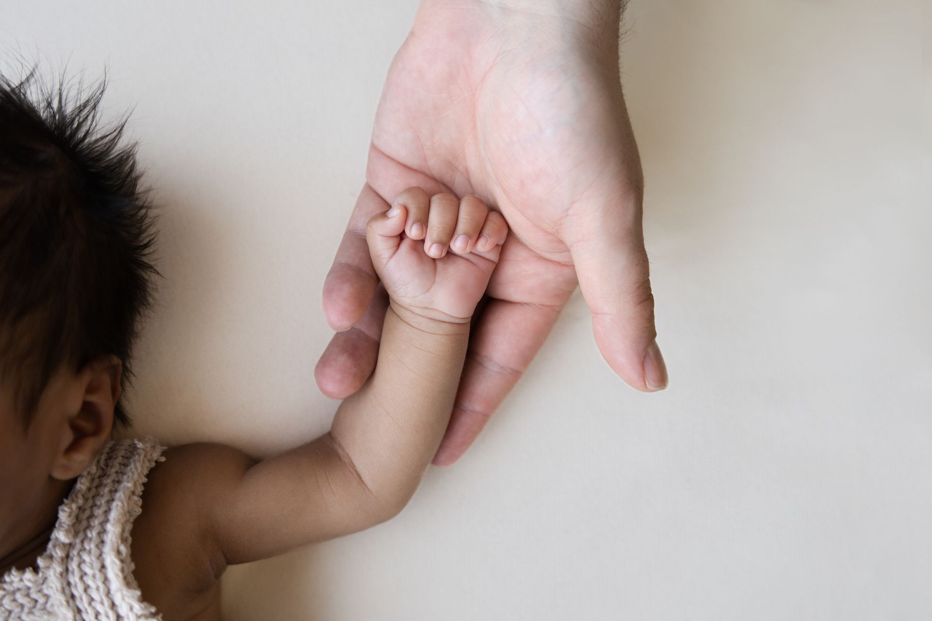 Een volwassene houdt de hand van een baby vast tegen een lichte achtergrond.
