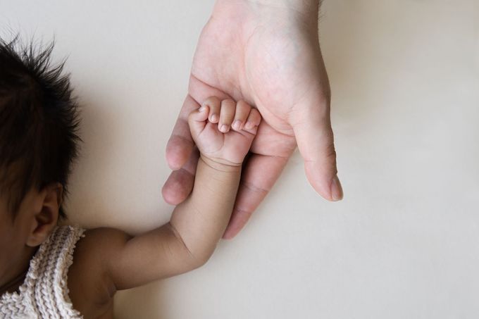 Een volwassene houdt de hand van een baby vast tegen een lichte achtergrond.