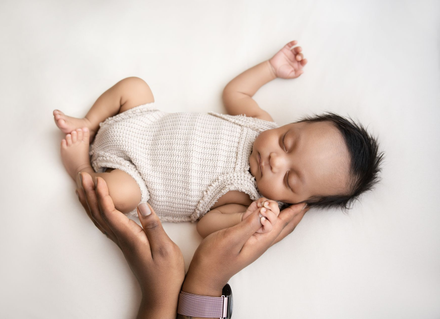 Slapende baby in een wit gebreid pakje, vastgehouden door een volwassene, tegen een witte achtergrond.