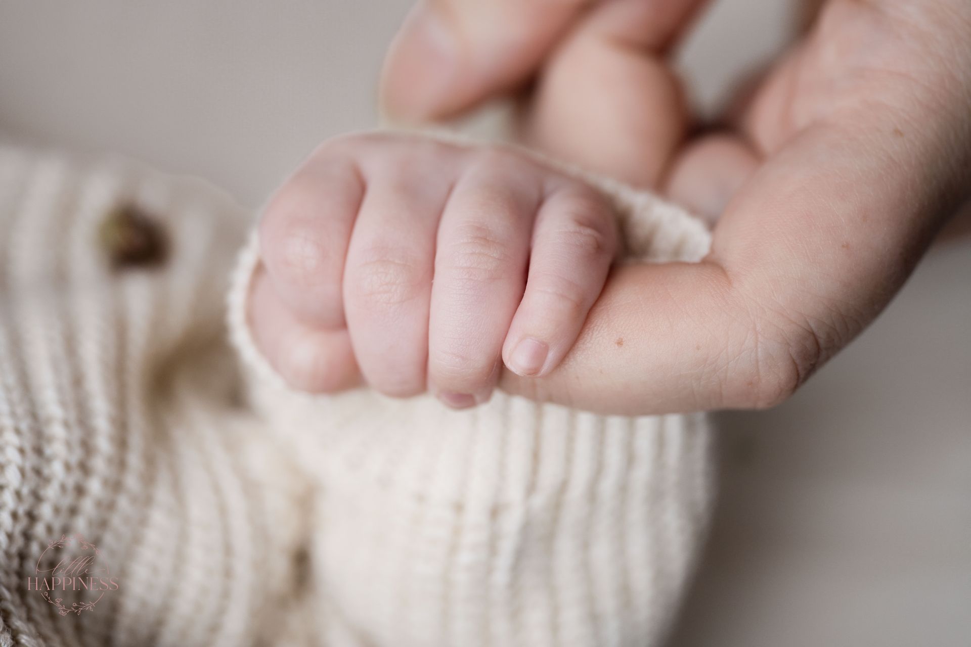 Een klein handje dat de vinger van een volwassene vasthoudt, van dichtbij gefilmd tegen een zachte beige deken.