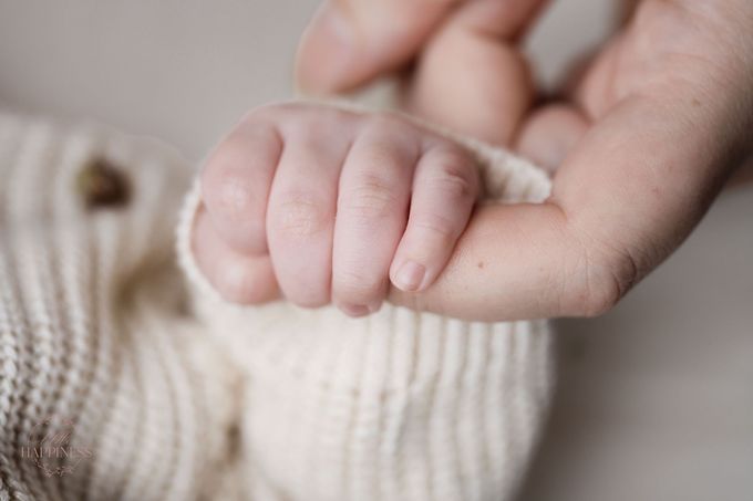 Een klein handje dat de vinger van een volwassene vasthoudt, van dichtbij gefilmd tegen een zachte beige deken.
