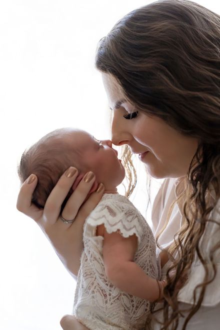 Een vrouw geeft een baby een teder kusje op de neus in een lichte, intieme binnenomgeving.